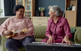 Two people are sitting on a couch, playing the ukulele and a keyboard respectively.