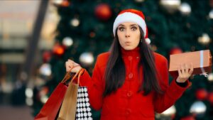 A woman with dark brown hair in a red coat and red and white hat holds multiple shopping bags.