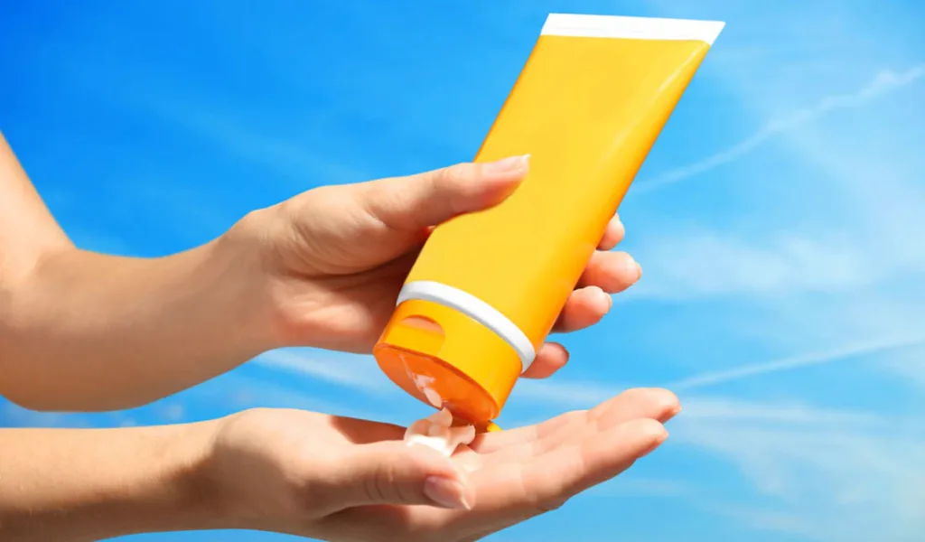 Someone squeezes sunscreen from an orange tube into their hand.