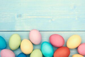 multi-colored Easter eggs lay against a baby blue wood panel.