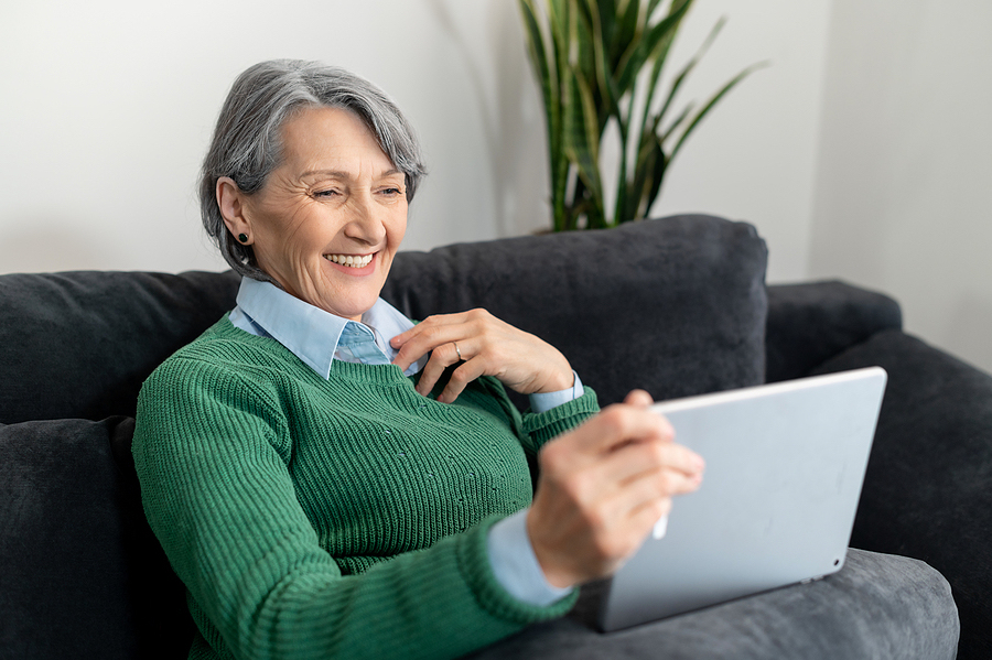 A Positive Senior Mature Woman Placed Her Hand On A Chest, Sitting On The Comfortable Couch, Holding