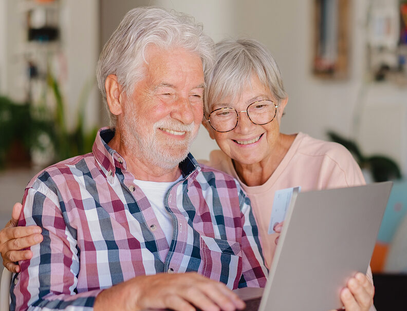Portrait Of Happy Modern Elderly Couple Browsing Together On Laptop