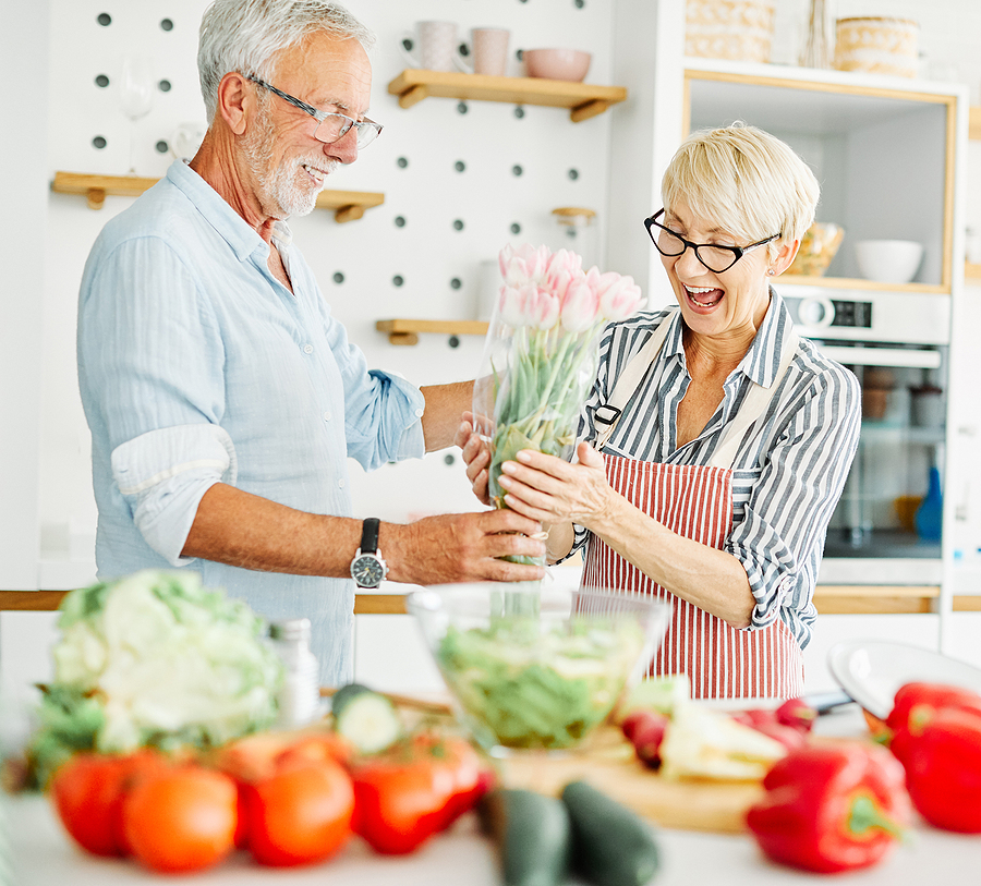 Portrait Of Happy Senior Couple With Flowers In Kitchen